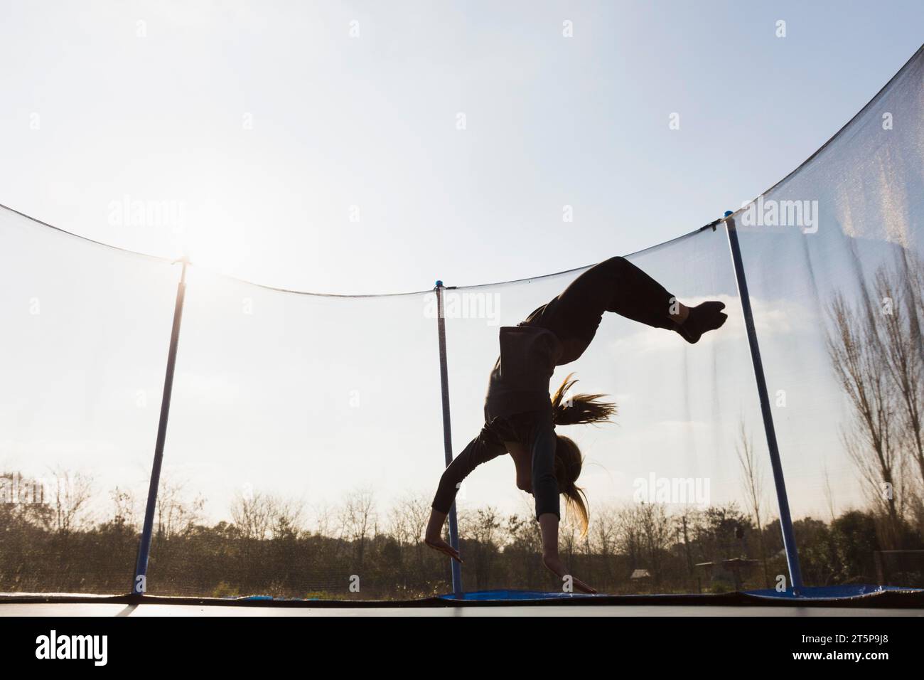 Silhouette fille sautant à l'envers trampoline contre le ciel bleu Banque D'Images