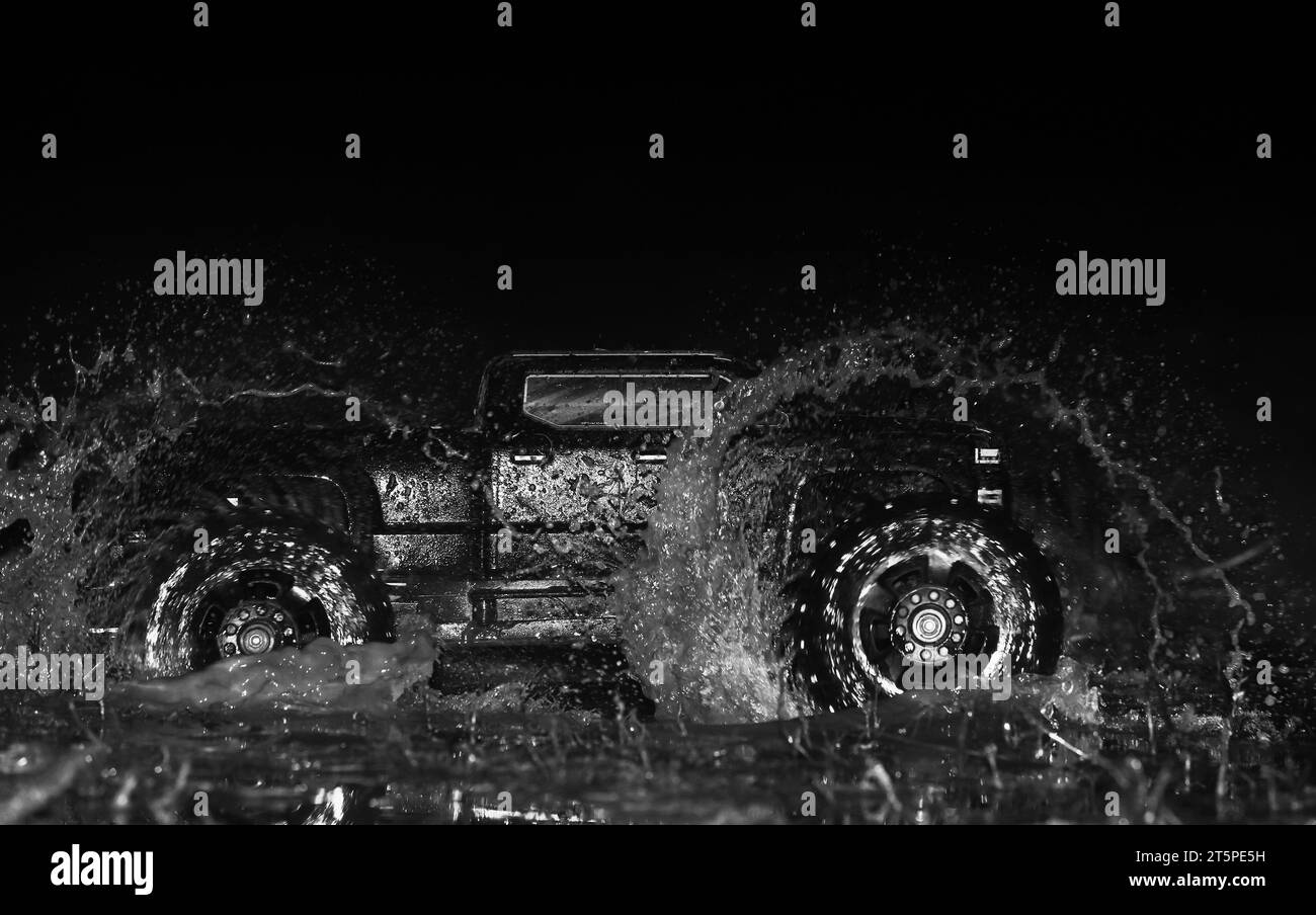 Modèle RC voiture éclaboussant de l'eau sur fond noir. Banque D'Images