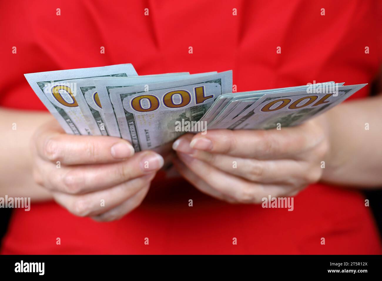 Dollars AMÉRICAINS dans la main féminine gros plan, femme en robe rouge compte l'argent. Concept de pot-de-vin, salaire, aide financière ou prêt Banque D'Images