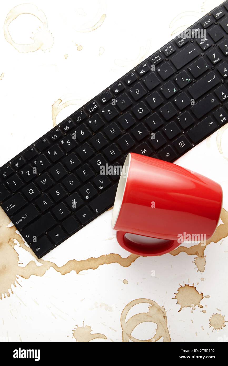 Un clavier d'ordinateur portable renversé et une tasse de café rouge renversée sur un fond blanc avec des taches de café. Banque D'Images Un clavier d'ordinateur portable renversé et une tasse de café rouge renversée sur un fond blanc avec des taches de café. Banque D'Images