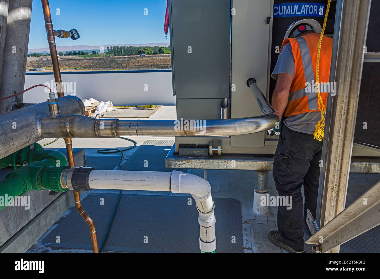 Un tuyau inoxydable nouvellement soudé et un ouvrier travaillant dans le panneau de compresseur d'un entrepôt de stockage de CO2 (réfrigération industrielle) sur le toit. Banque D'Images