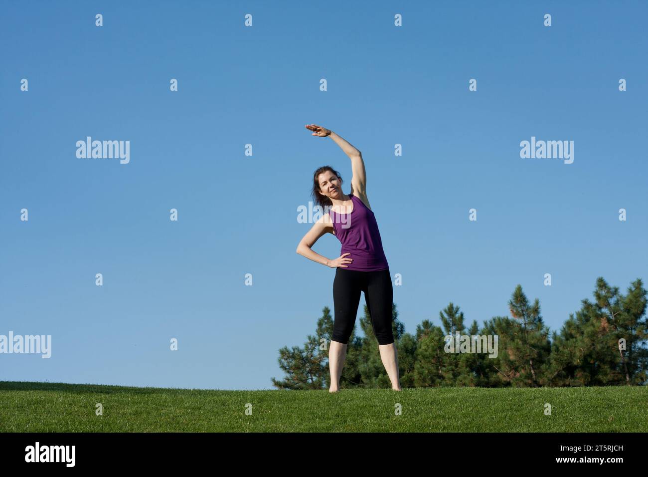 Jeune femme athlétique faisant l'échauffement avant l'entraînement de fitness dans le parc, fond de ciel bleu. Belle femme pratique le yoga, Pilates, debout pieds nus Banque D'Images