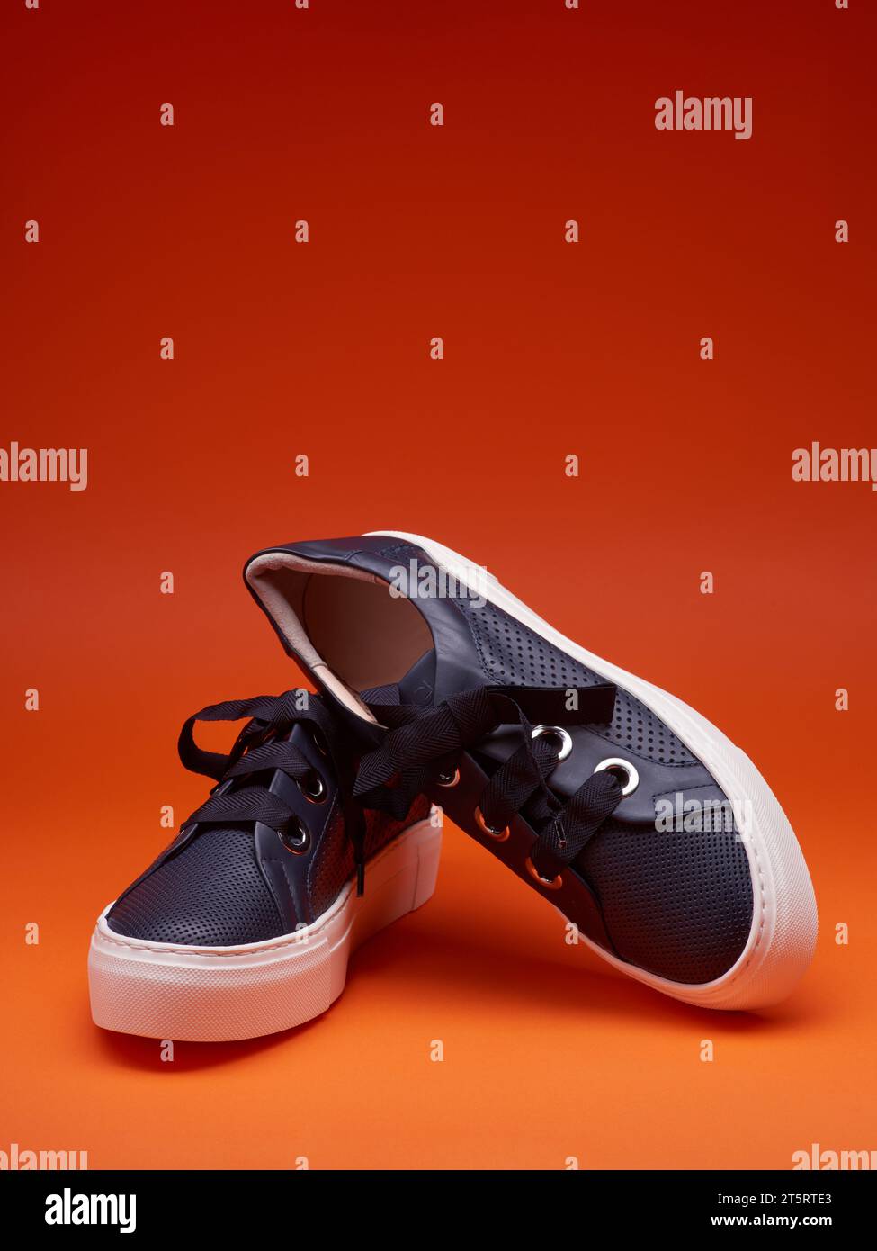 Baskets élégantes et décontractées bleu marine avec des semelles blanches épaisses et de larges lacets, isolées sur un fond rouge-orange vif avec espace de copie pour le texte. Adve Banque D'Images