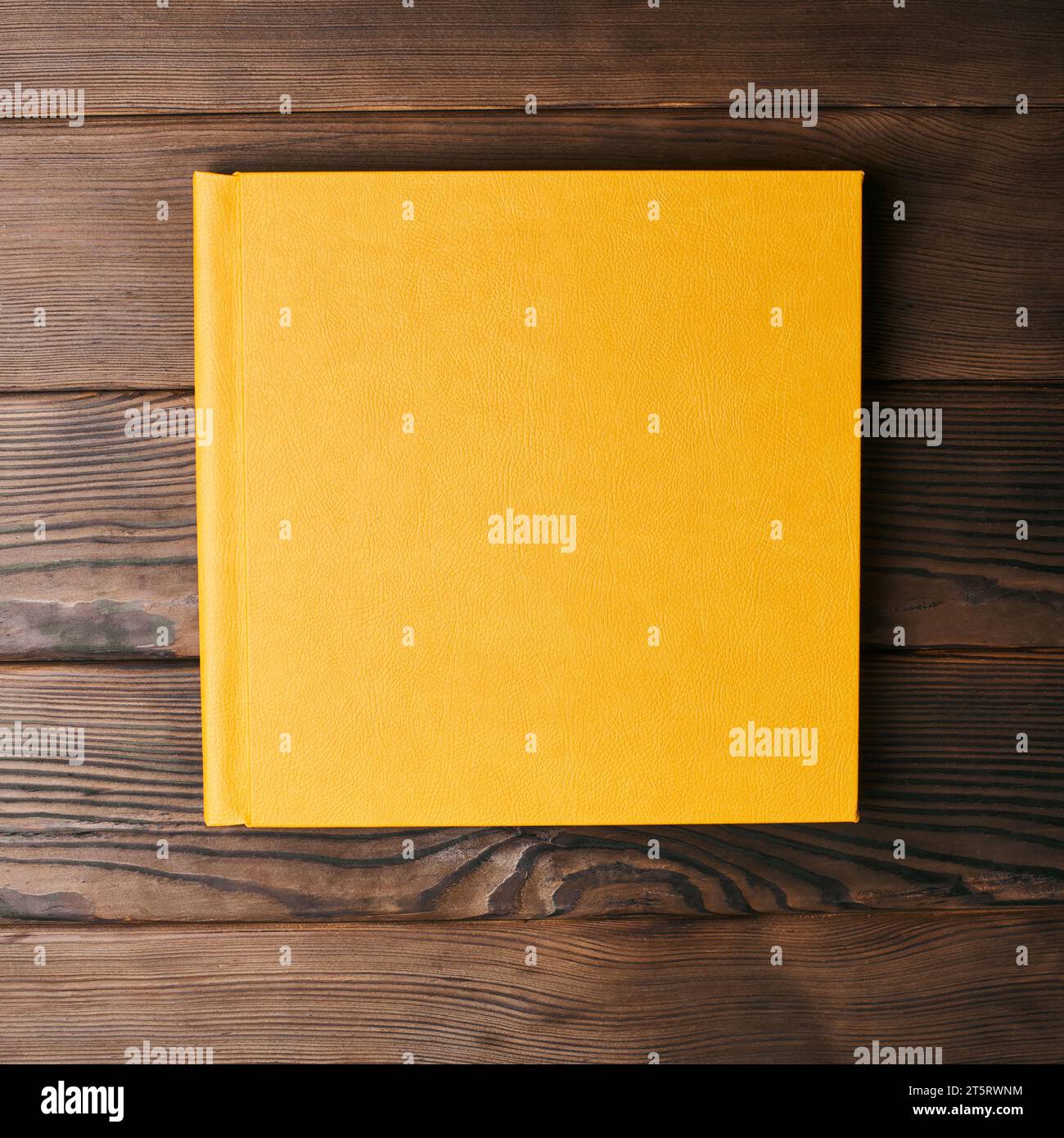 Livre photo relié en cuir jaune isolé sur un fond en bois avec espace de copie. Vue de dessus, pose à plat. Сlosed maquette de reliure de livre pour ajouter personnel Banque D'Images