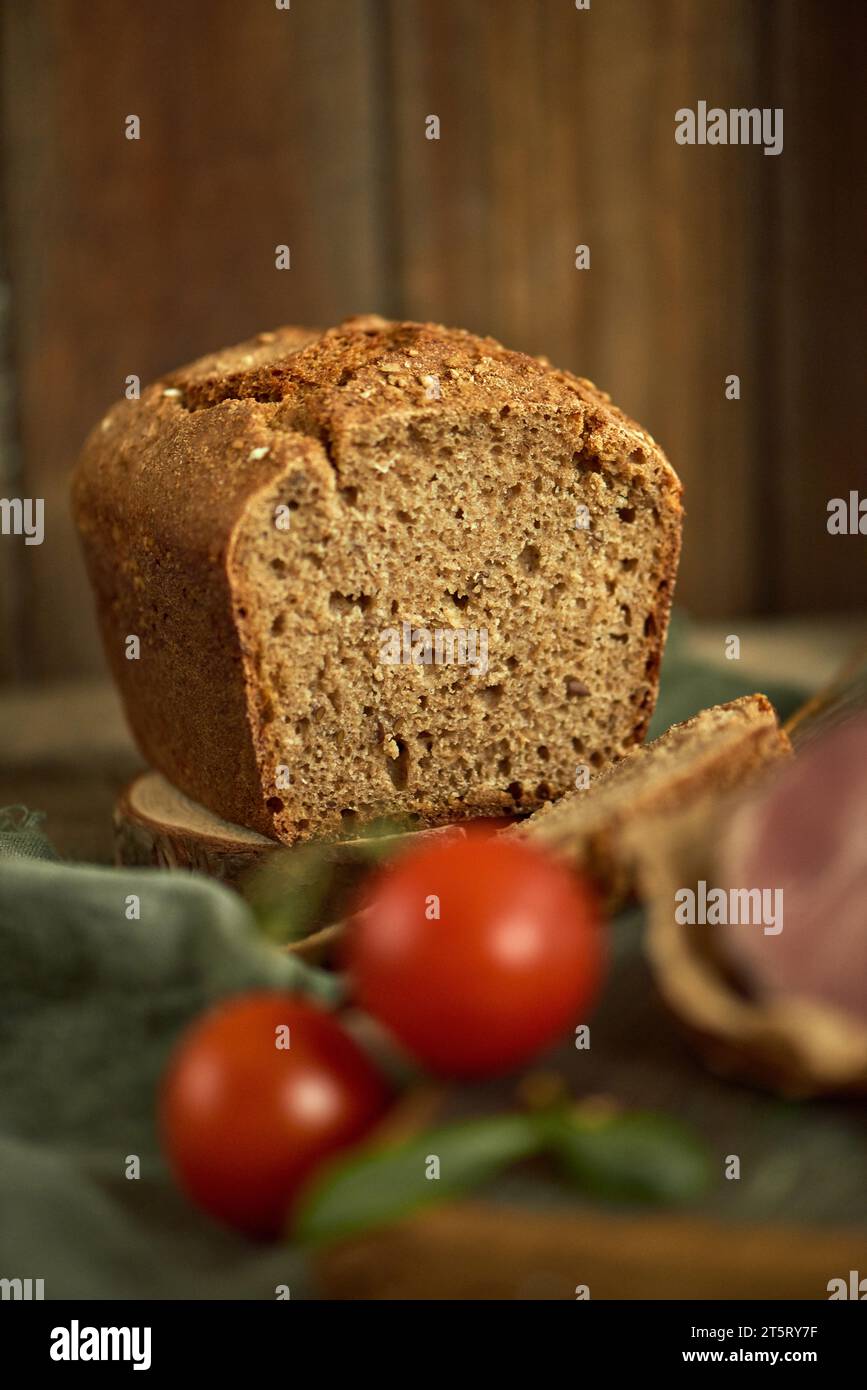 Une miche de pain de blé entier frais maison. Les tomates et le jambon sont flous au premier plan. Concept d'alimentation saine. Aliments biologiques nutritifs. A. Banque D'Images