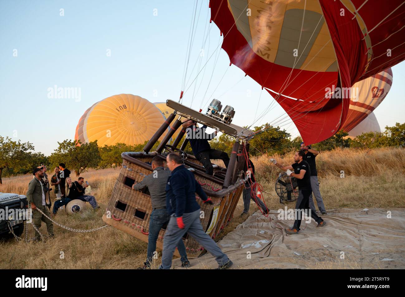 L'équipage allume les brûleurs, soulevant le ballon et le panier en osier pour un voyage au lever du soleil sur les paysages de Cappadoce. Banque D'Images