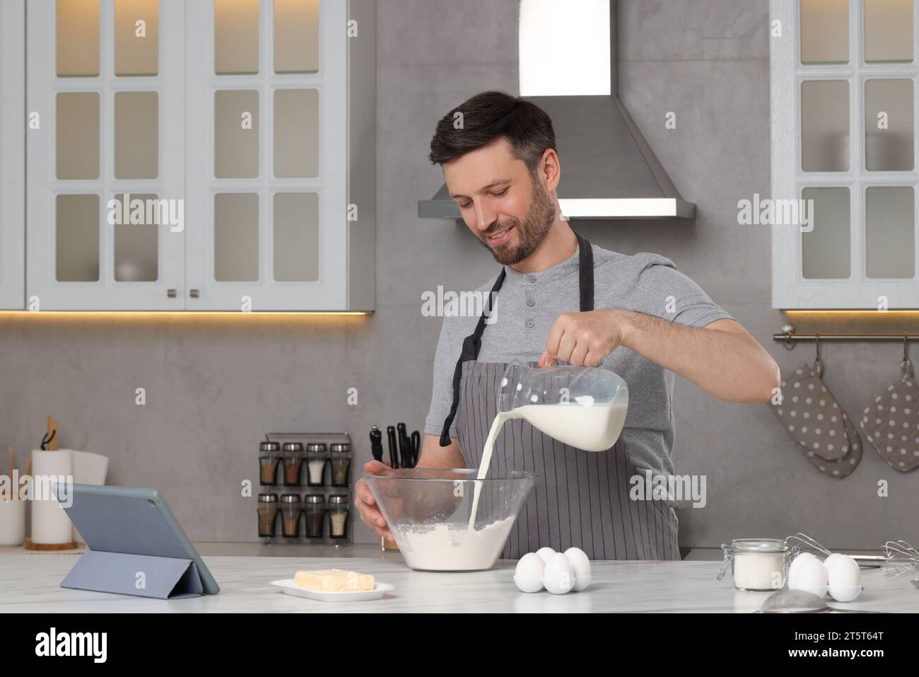 Homme heureux lisant la recette sur tablette tout en cuisinant dans la cuisine. Livre culinaire en ligne Banque D'Images