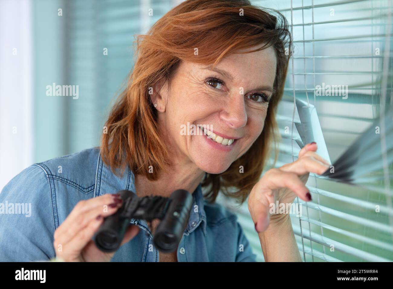 femme regarde et fouille avec des jumelles par une fenêtre Banque D'Images