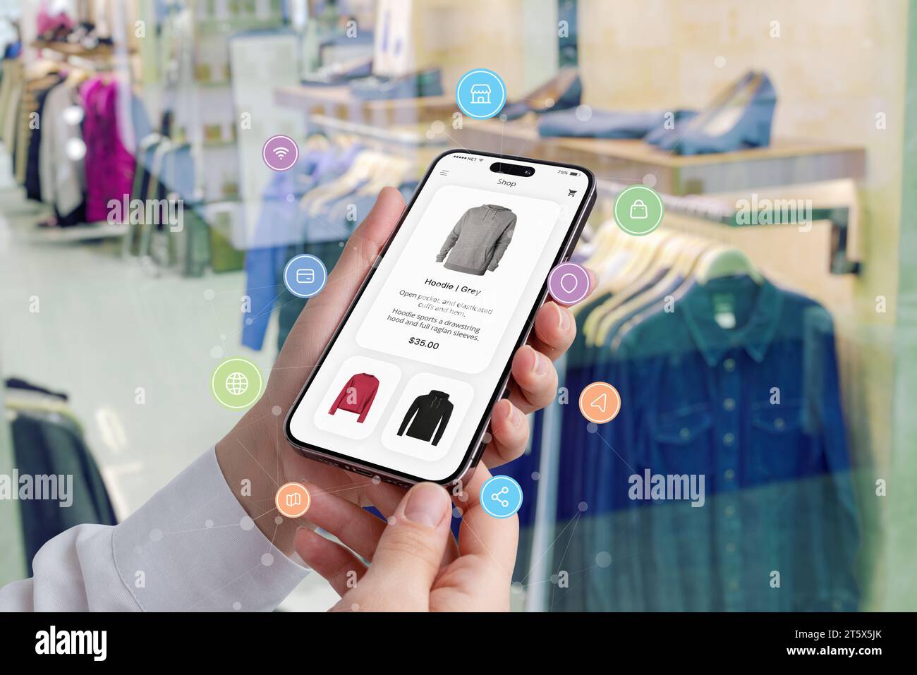 Les mains des femmes tiennent un smartphone avec une application shopping entourée d'icônes de shopping, tandis qu'une boutique présente des vêtements en arrière-plan Banque D'Images