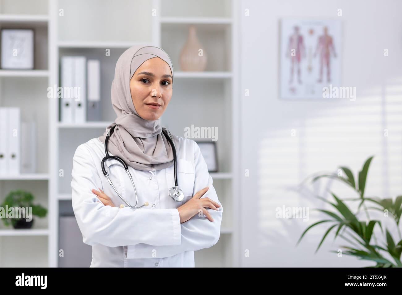 Portrait de la femme médecin réussie sérieuse confiante dans le hijab dans le manteau médical blanc regardant la caméra avec les bras croisés, travailleur de la clinique travaillant à l'intérieur de la salle médicale de bureau. Banque D'Images