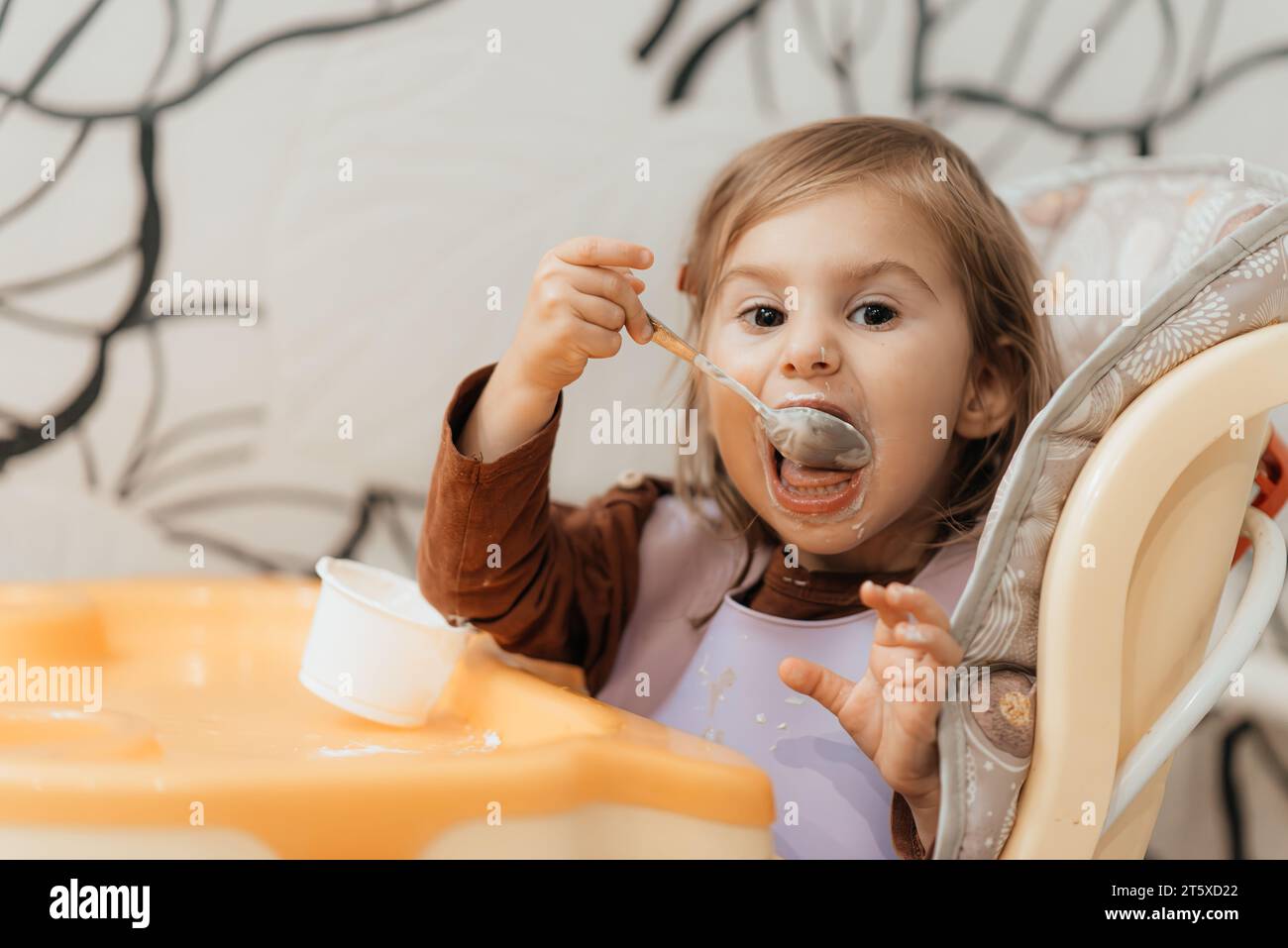 Cute little girl eating yoghurt à l'intérieur de l'enfant Banque D'Images