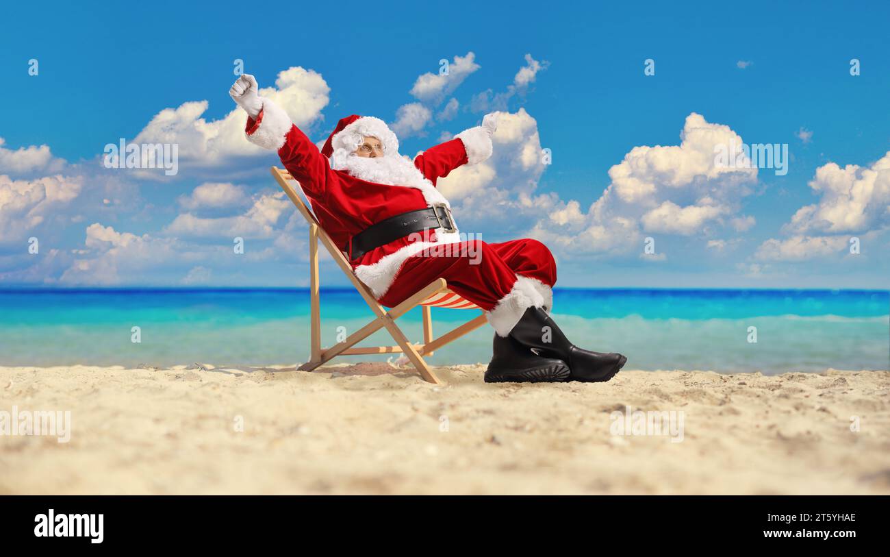 Excité Père noël profiter de vacances d'été sur une chaise longue assis à la plage au bord de la mer Banque D'Images