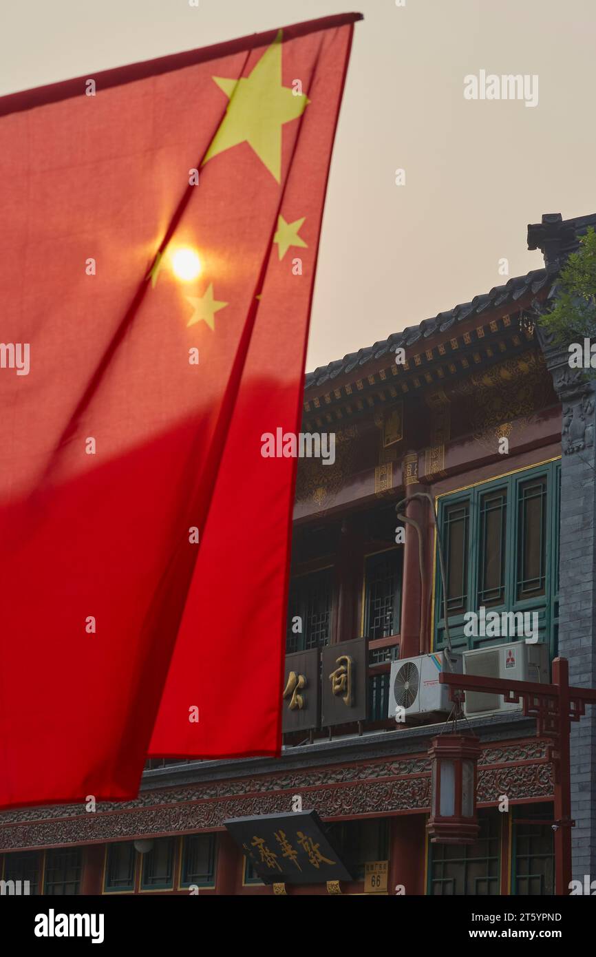 Soleil brillant à travers le drapeau national de la Chine (drapeau rouge cinq étoiles) volant après le lever du soleil à Da Shi LAN, Pékin, Chine. Banque D'Images