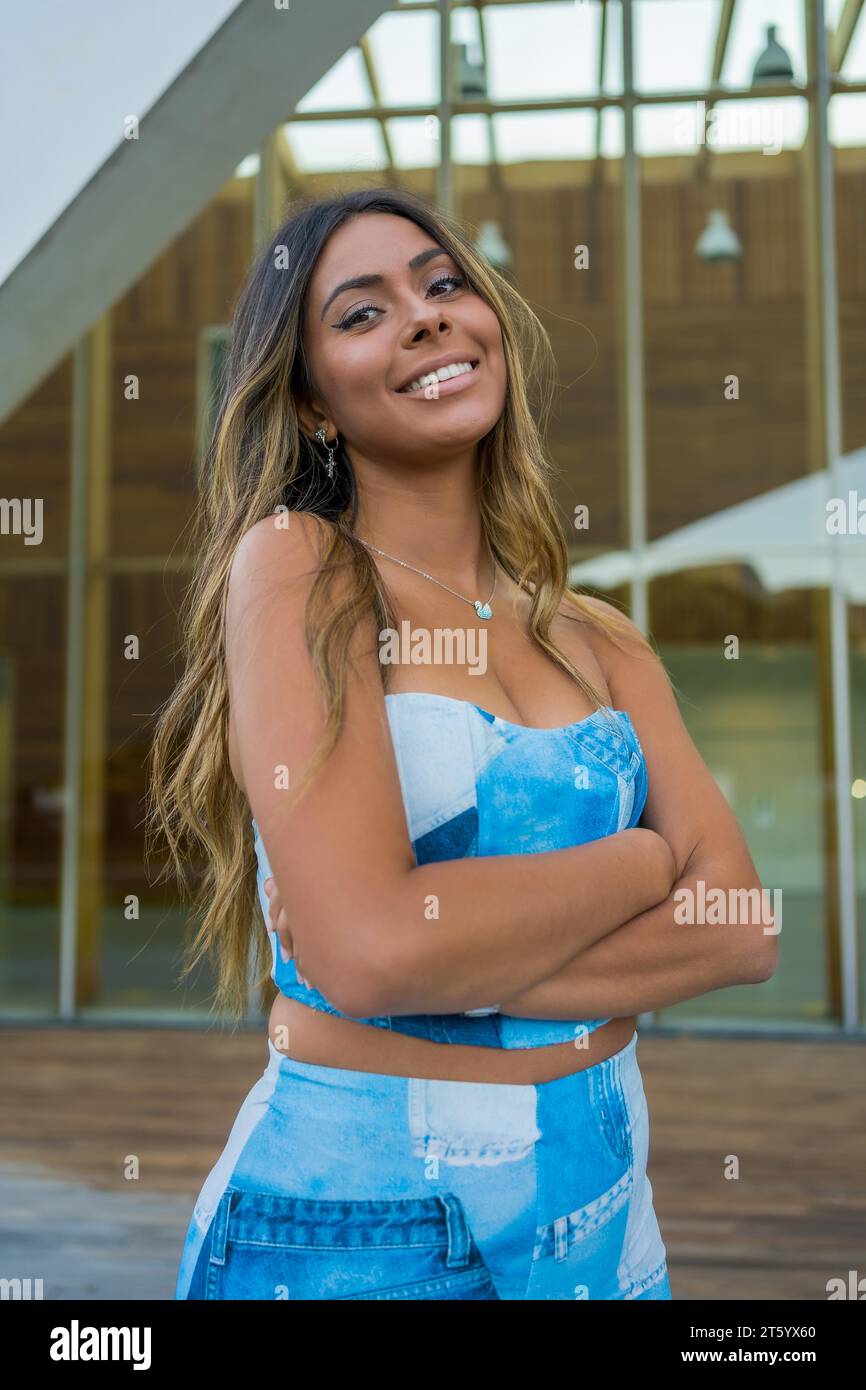 Photo verticale d'une jolie femme en vêtements denim debout avec le bras croisé souriant à la caméra Banque D'Images
