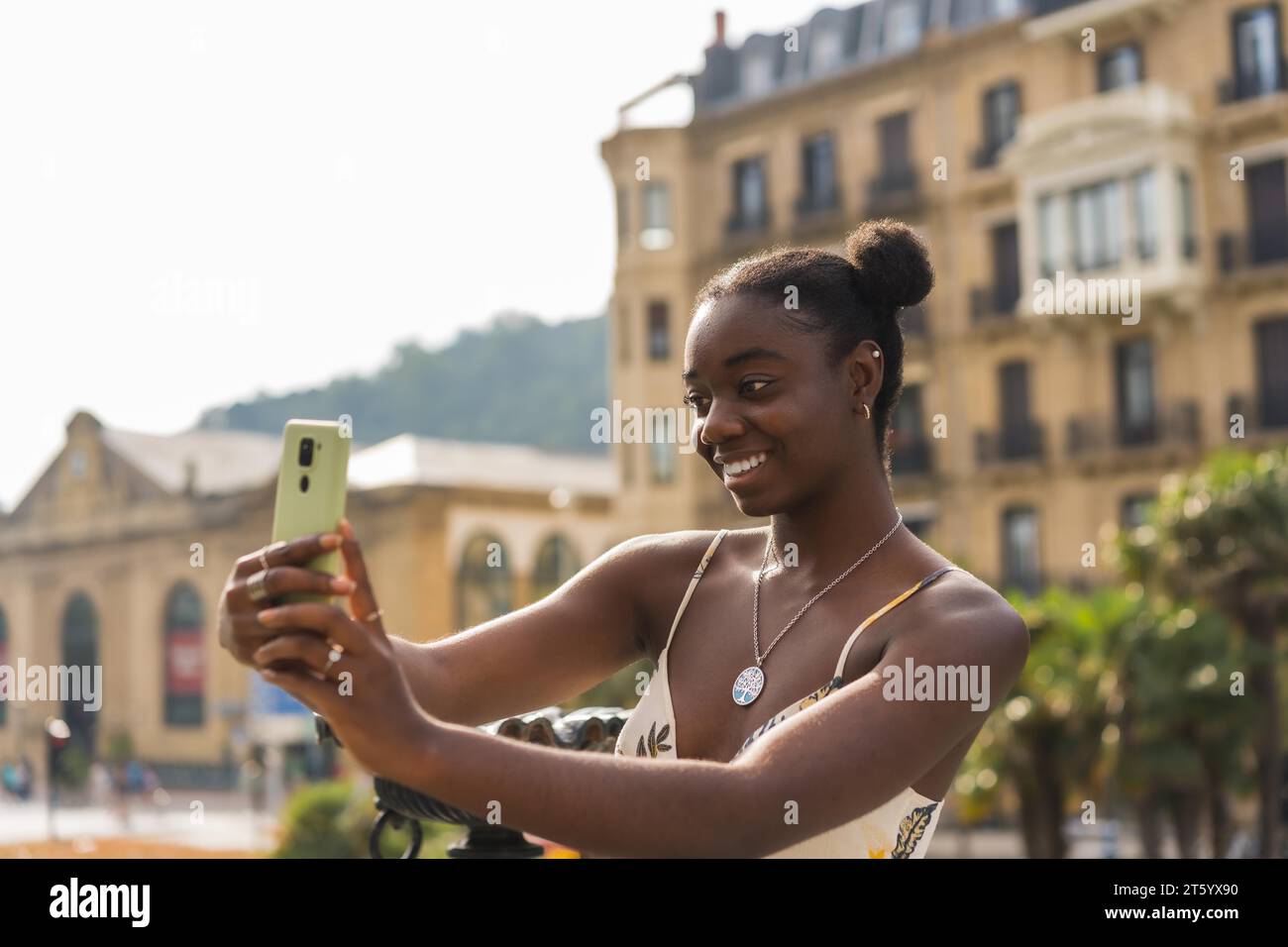 Vue latérale d'une jolie jeune femme africaine prenant un selfie dans la rue Banque D'Images