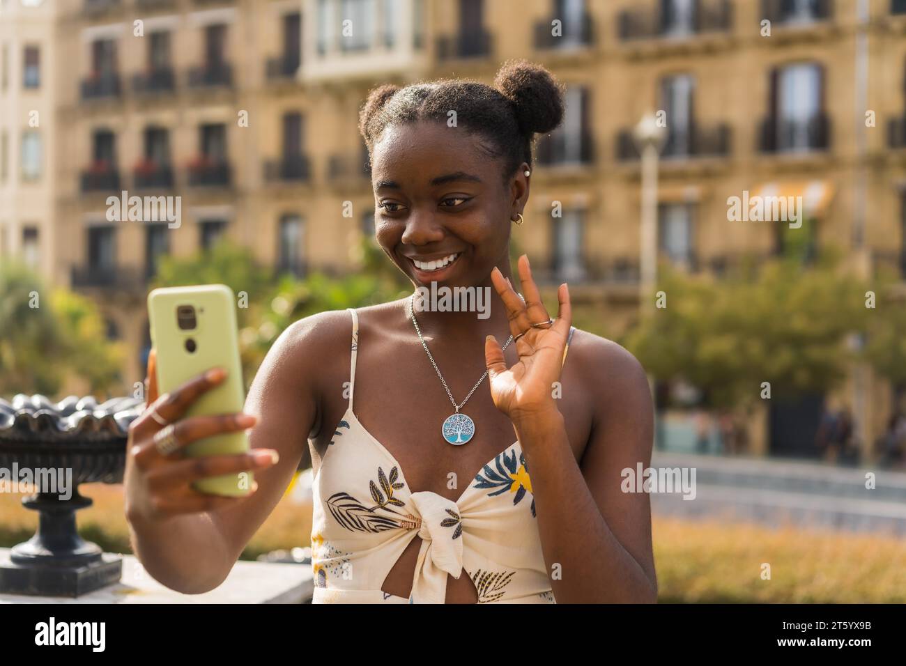 Jeune femme africaine mignonne agitant pendant un appel vidéo avec le téléphone portable dans la rue Banque D'Images