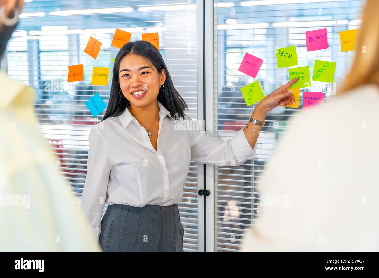 Heureuse femme chinoise à côté d'un verre avec des notes adhésives expliquant des idées à des collègues Banque D'Images