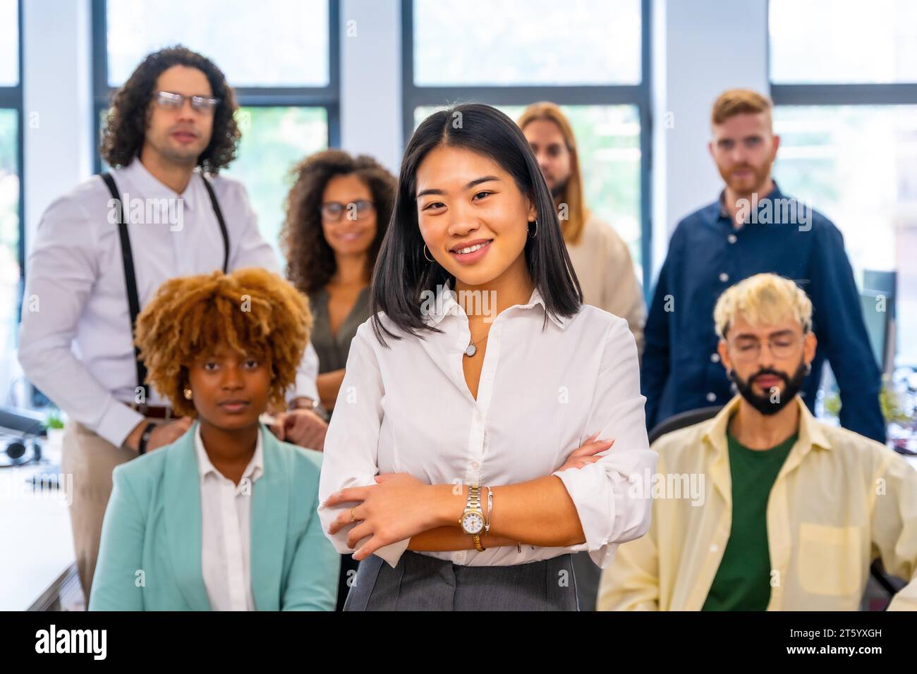 Fier entrepreneur chinois debout avec les bras croisés à côté de collègues dans le bureau Banque D'Images