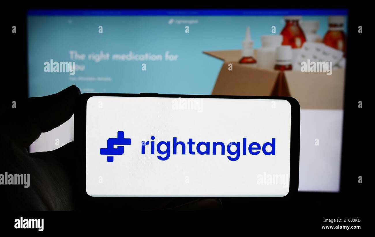 Personne tenant le smartphone avec le logo de la société britannique de pharmacie en ligne Rightangled Limited en face du site Web. Concentrez-vous sur l'affichage du téléphone. Banque D'Images