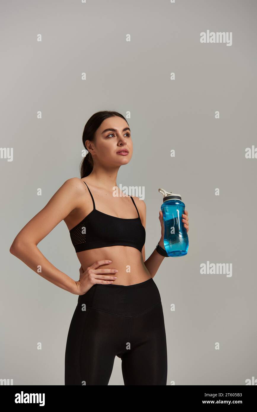 slim sportswoman en leggings et crop top tenant la bouteille avec de l'eau tout en se tenant debout avec les mains sur la hanche Banque D'Images