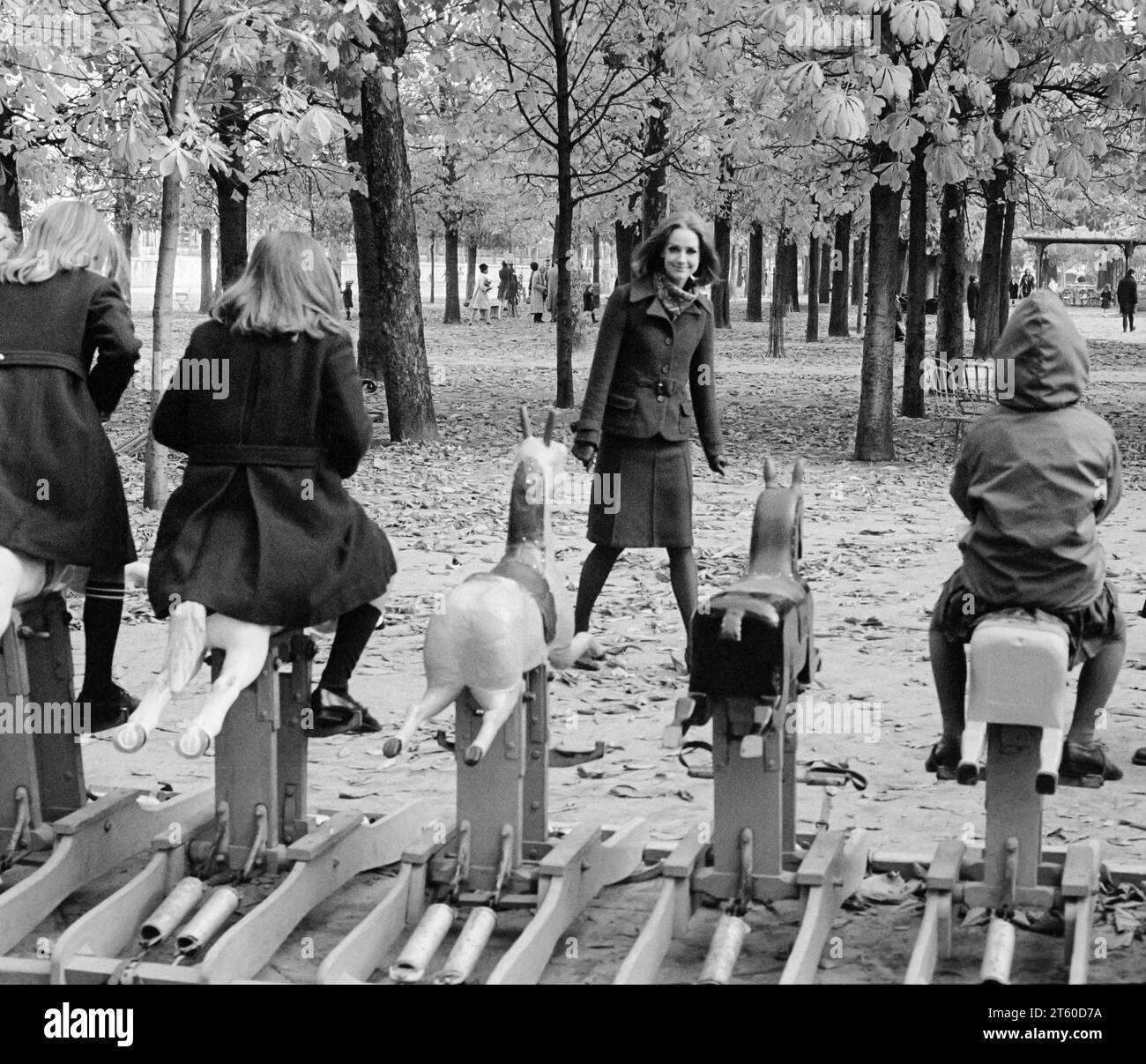Années 1960, mannequin femme regarde des enfants jouant sur un carrousel de chevaux, jardin des Tuileries, Paris, France, Europe, Banque D'Images