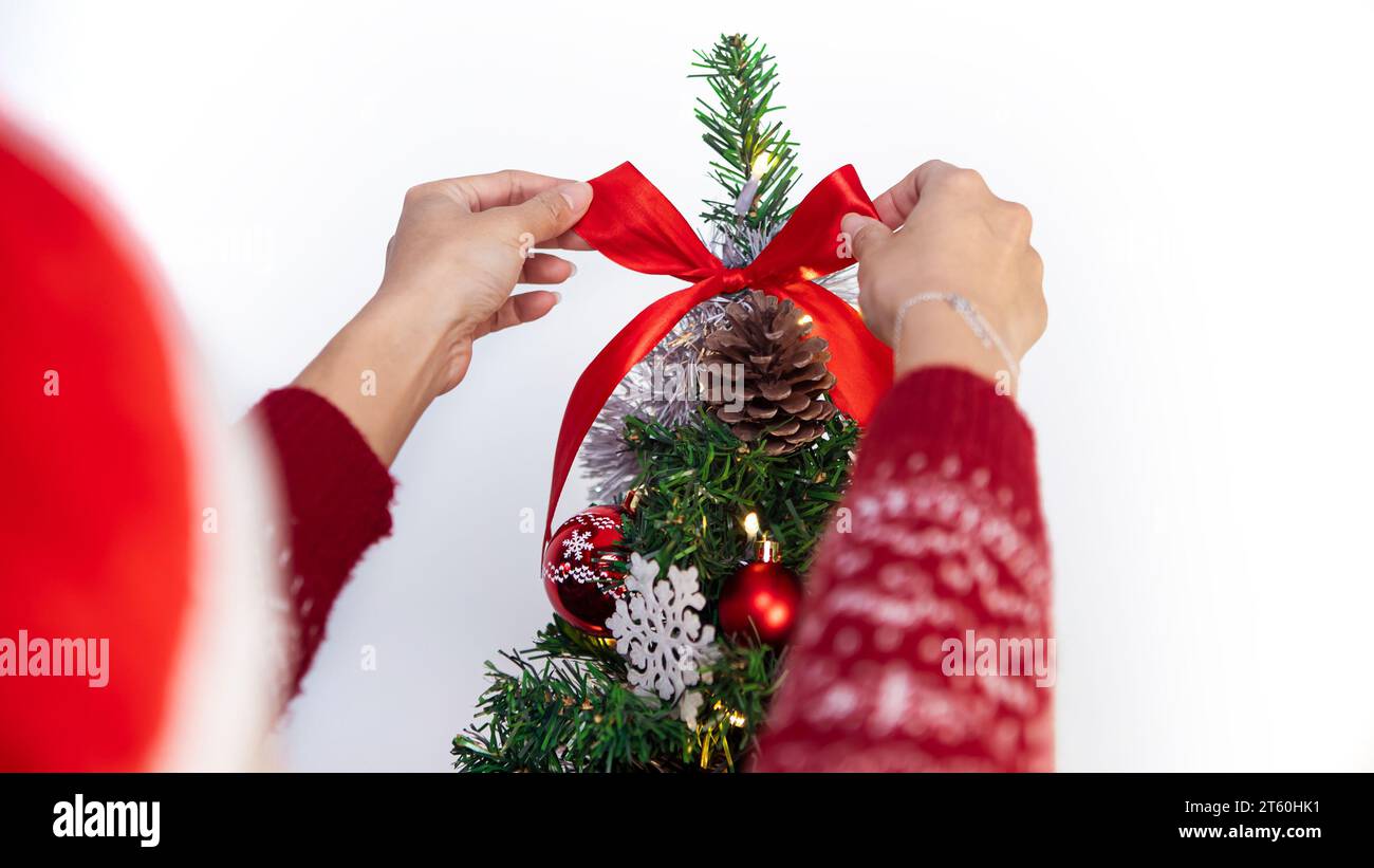 Femme asiatique décorant l'arbre de noël avec l'arc rouge dans la maison de salon. Joyeux noël et bonne année concept. Fille mettant ruban ornement de Noël Banque D'Images