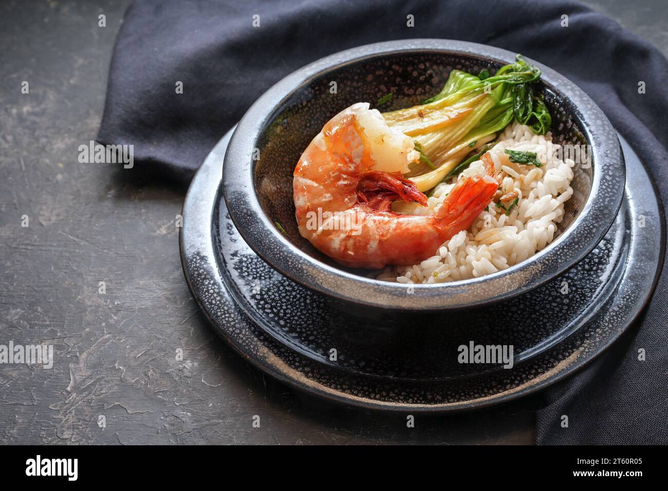 Crevettes géantes frites ou crevettes avec riz et pak choi dans un bol en céramique tachetée noire sur un fond sombre, cuisine dans un style asiatique, espace copie, sélectionné Banque D'Images