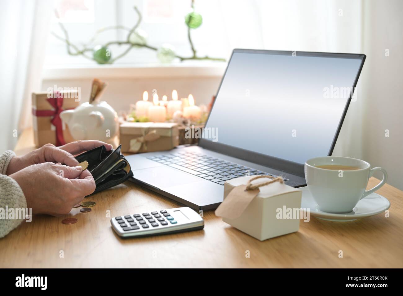 Chers achats en ligne de Noël, mains d'une femme plus âgée comptant l'argent sur une table avec ordinateur portable, cadeaux, bougies, tirelire et calculatrice, copie sp Banque D'Images