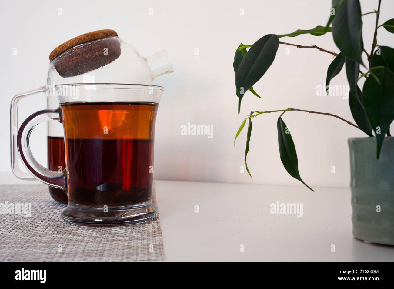 Thé noir dans une tasse en verre et théière en verre fraîchement infusée sur une serviette et feuilles vertes avec fond blanc Banque D'Images
