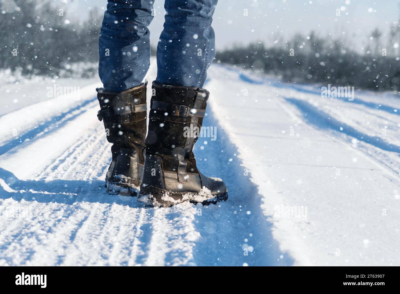 Un voyageur en bottes marche le long d'une route hivernale enneigée. Banque D'Images