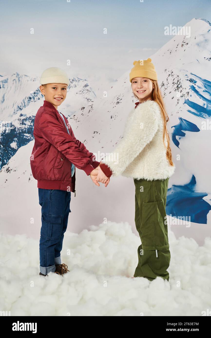 mignons amis préadolescents dans des vestes d'hiver élégantes et des chapeaux de bonnet tenant les mains et souriant à l'appareil photo Banque D'Images