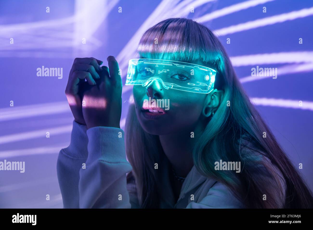 Jeune femme sans émotion hypnotisée par des lunettes LED VR modernes et immergée dans l'expérience de réalité virtuelle sur des lumières de projecteur éclairées Banque D'Images
