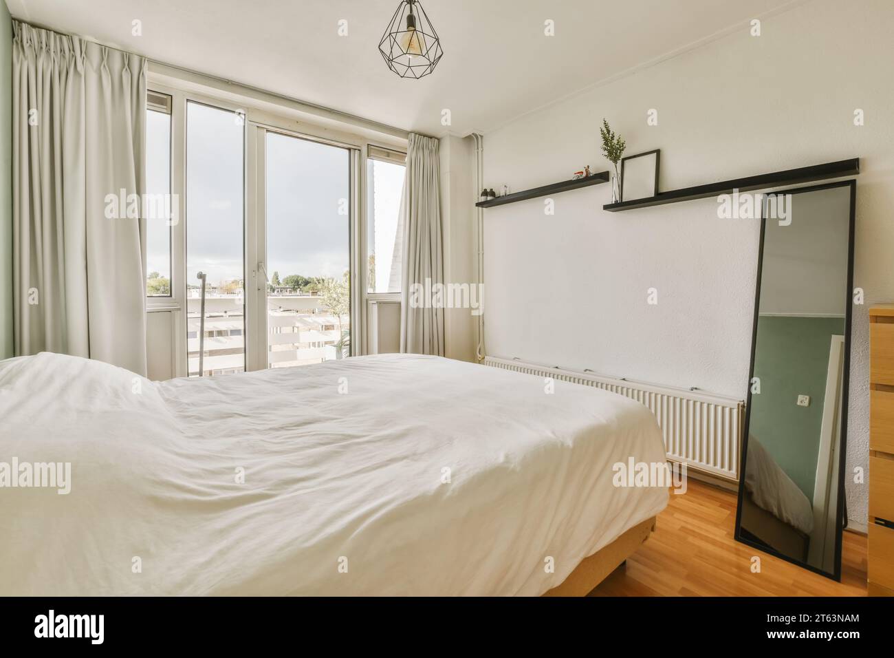 Intérieur de la chambre moderne avec lit blanc confortable et miroir avec grande fenêtre dans la maison blanche contemporaine Banque D'Images