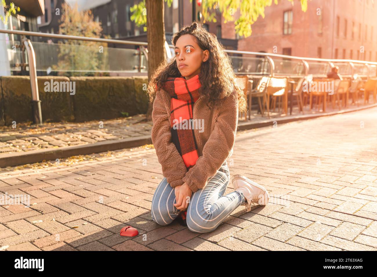 femme bouleversée avec les cheveux longs en écharpe orange et veste assise sur le steet. Femme tenant un cœur brisé rouge. Obtenir un concept de divorce Banque D'Images