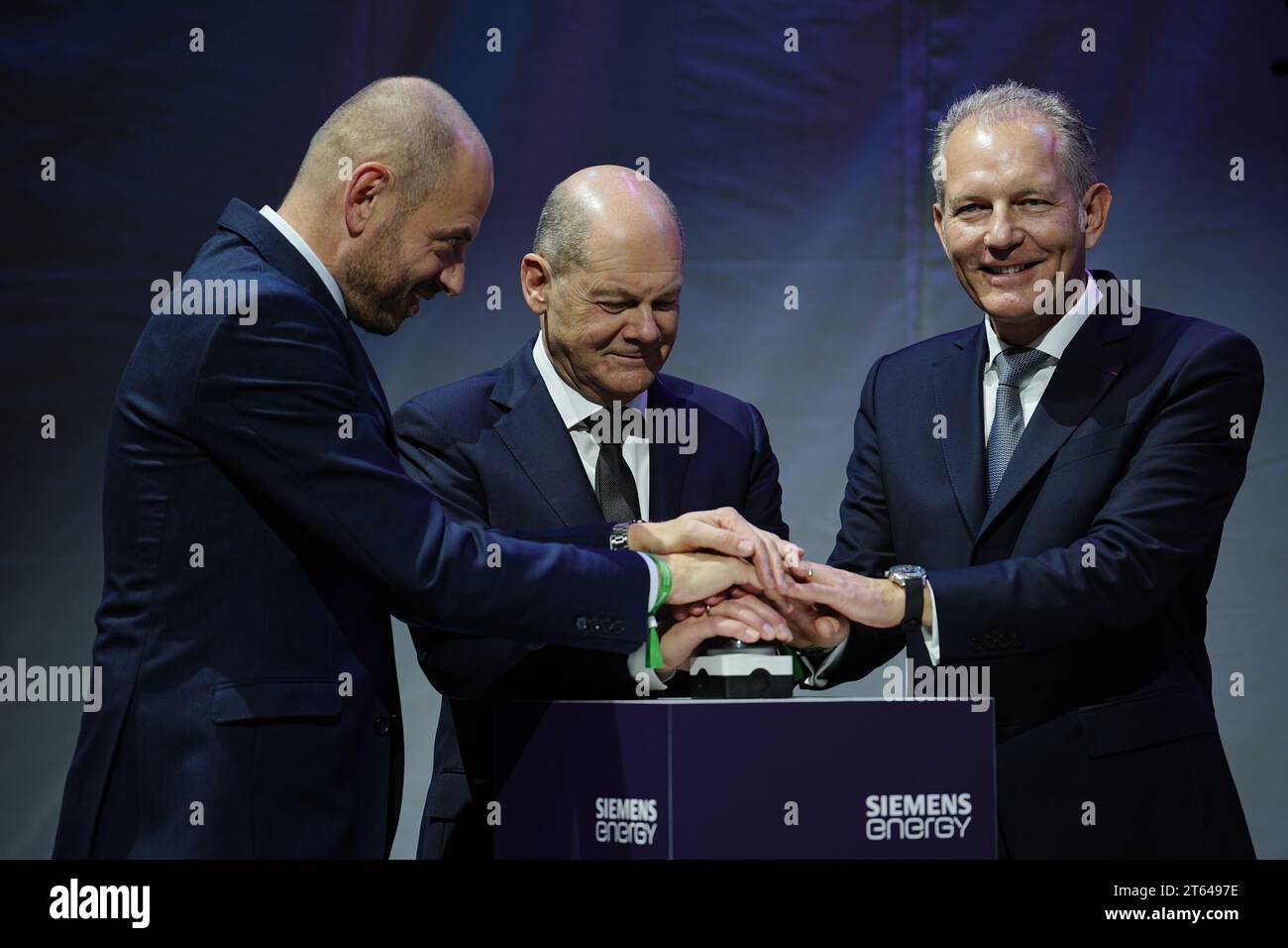 Berlin, Allemagne. 08 novembre 2023. Le chancelier allemand OLAF Scholz (M, SPD) appuie sur un bouton pour ouvrir le site de production d'électrolyseurs de Siemens Energy avec Christian Bruch (l), PDG de Siemens Energy, et François Jackow, PDG d'Air liquide. D’ici 2025, au moins trois gigawatts de capacité d’électrolyse seront mis sur le marché chaque année à partir de la nouvelle installation de production, jetant ainsi les bases de la montée en puissance de l’industrie de l’hydrogène vert. L'usine de production de plusieurs gigawatts fournira des projets d'hydrogène dans le monde entier depuis Berlin. Crédit : Kay Nietfeld/dpa/Alamy Live News Banque D'Images