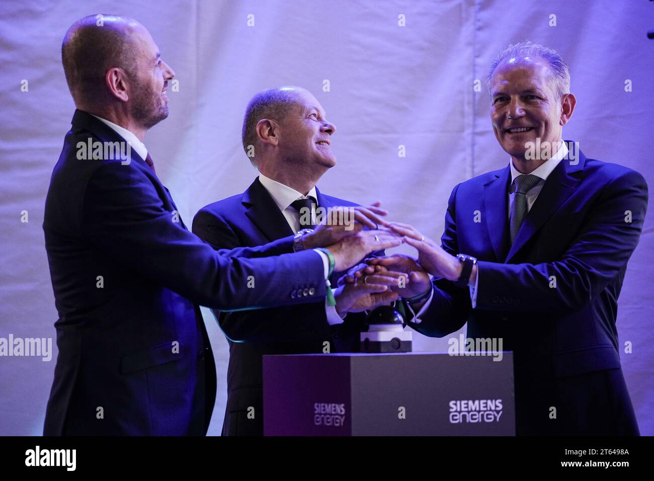 Berlin, Allemagne. 08 novembre 2023. Le chancelier allemand OLAF Scholz (M, SPD) appuie sur un bouton pour ouvrir le site de production d'électrolyseurs de Siemens Energy avec Christian Bruch (l), PDG de Siemens Energy, et François Jackow, PDG d'Air liquide. D’ici 2025, au moins trois gigawatts de capacité d’électrolyse seront mis sur le marché chaque année à partir de la nouvelle installation de production, jetant ainsi les bases de la montée en puissance de l’industrie de l’hydrogène vert. L'usine de production de plusieurs gigawatts fournira des projets d'hydrogène dans le monde entier depuis Berlin. Crédit : Kay Nietfeld/dpa/Alamy Live News Banque D'Images