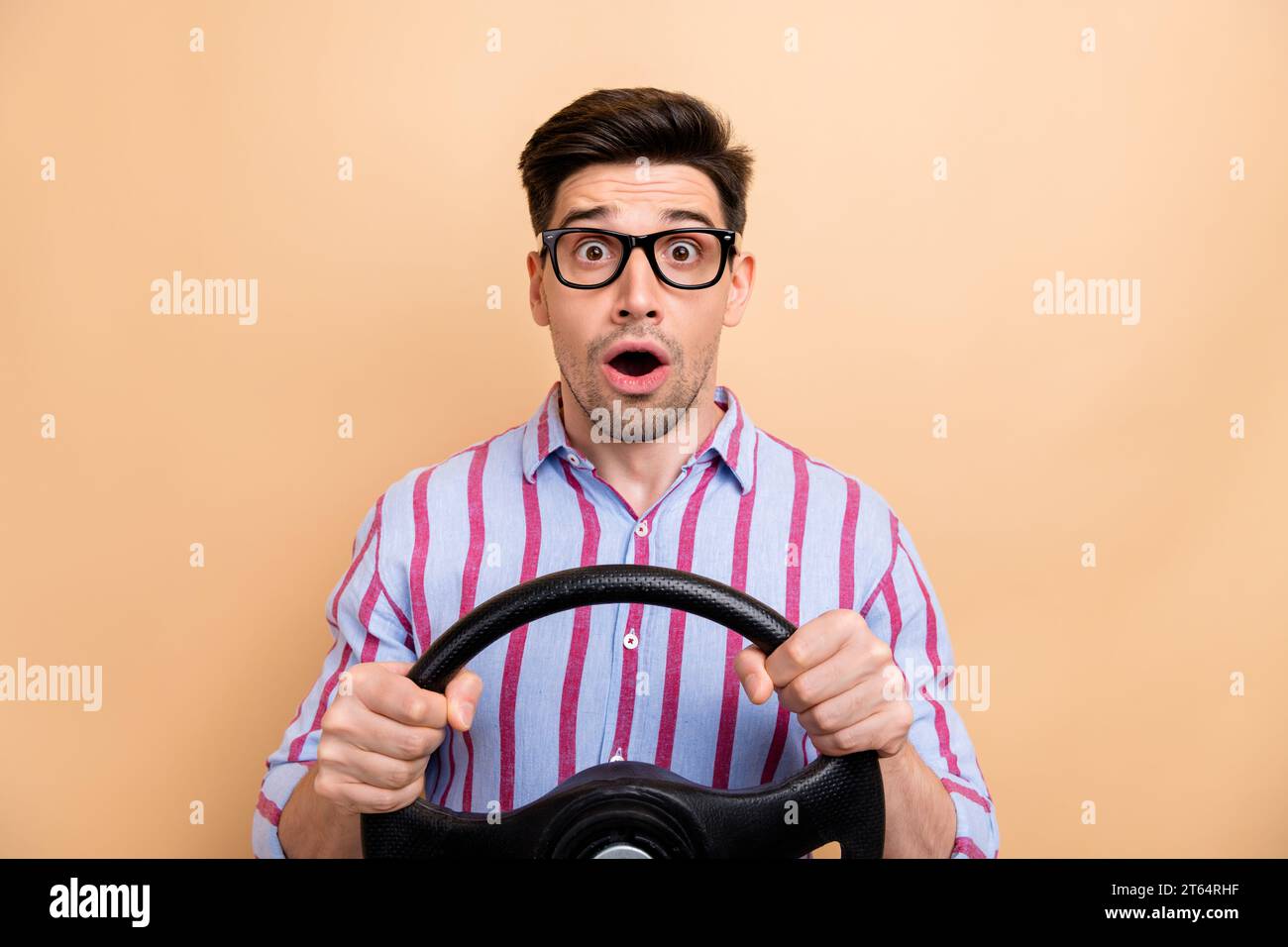 Photo de jeune homme drôle choqué regardant tenant le volant inattendu première fois accident de voiture isolé sur fond de couleur beige Banque D'Images