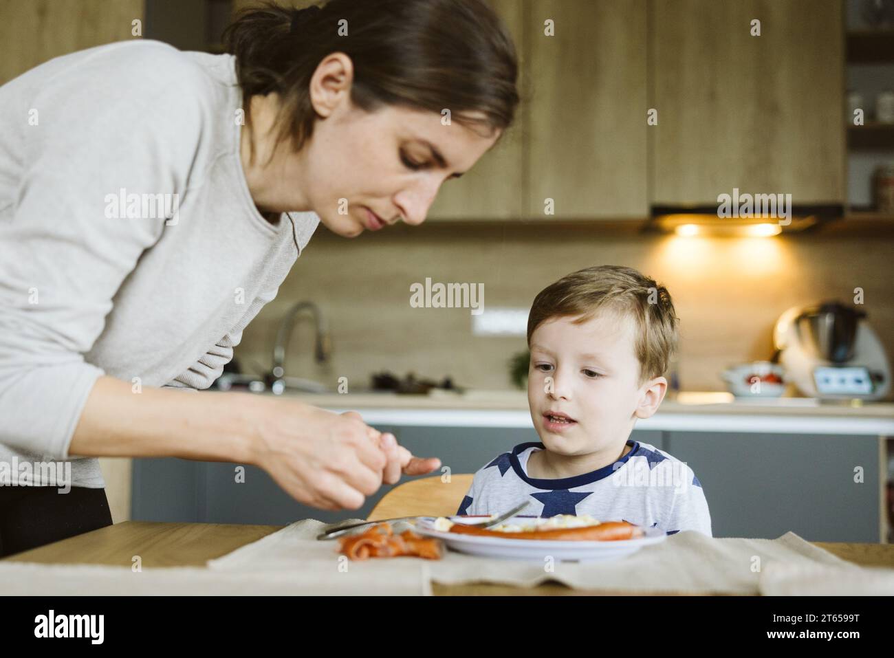 Mère nourrissant amoureusement son fils petit déjeuner bio dans la cuisine Banque D'Images