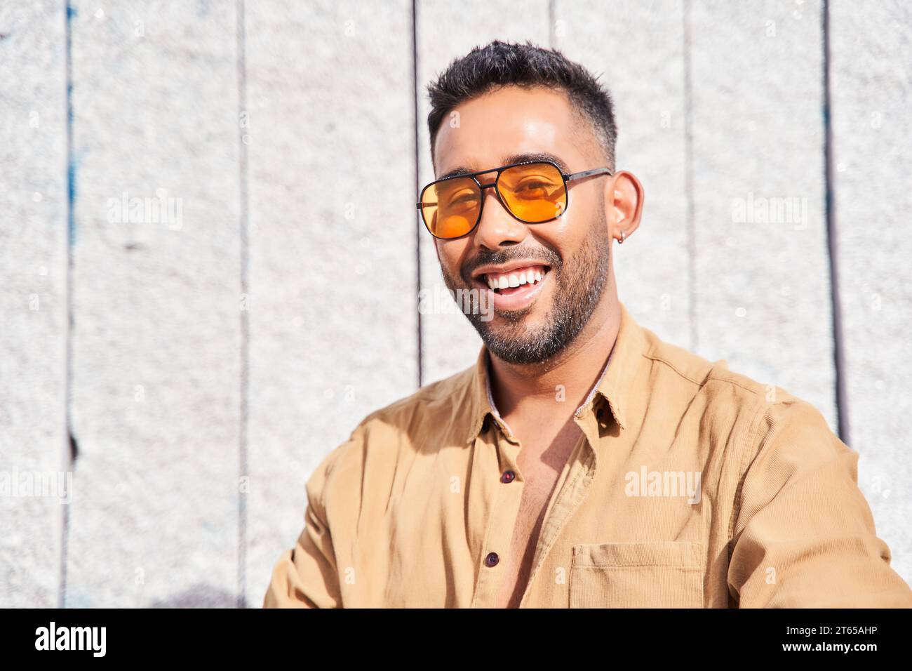 jeune homme à la mode avec des lunettes de soleil orange et barbe souriante. homme latin regardant la caméra avec des dents parfaites. Banque D'Images