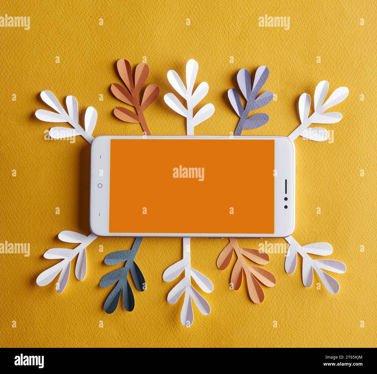 Un téléphone portable blanc avec un espace blanc orange vide pour le texte au milieu repose sur un fond jaune entouré de feuilles de papier de blanc, bleu et Banque D'Images