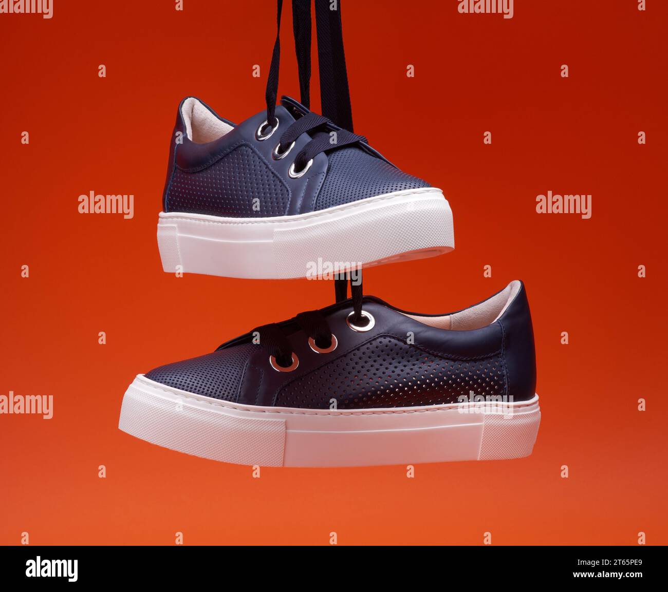 Paire de chaussures tendance décontractée bleu marine accrochées devant un fond orange vif. Cuir perforé, lacets épais, œillets métalliques. Blog de mode ou Banque D'Images