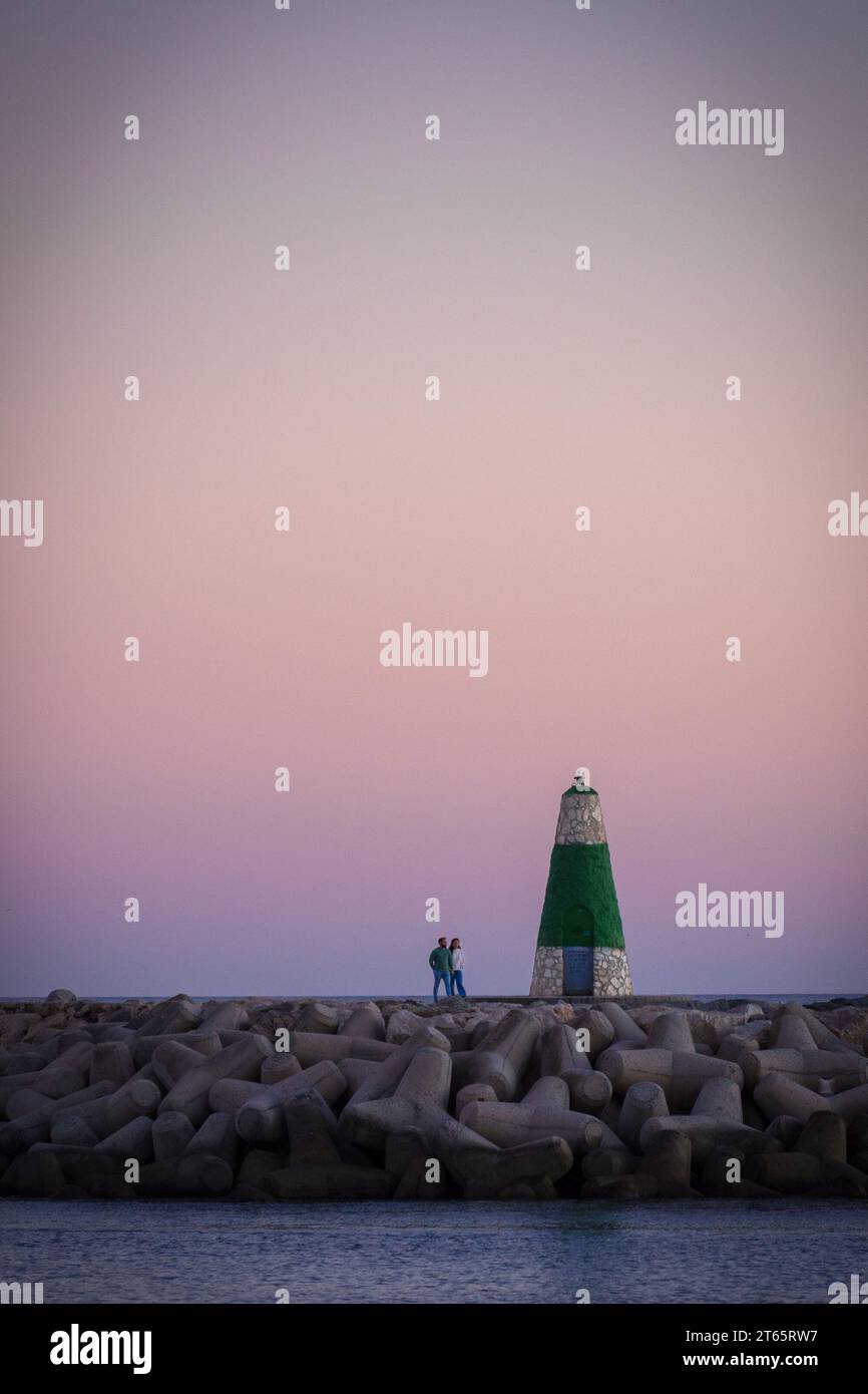 Benalmádena, Espagne - novembre 26 2022 : couple marchant à côté d'un phare sur des brise-lames au coucher du soleil à Benalmádena Banque D'Images