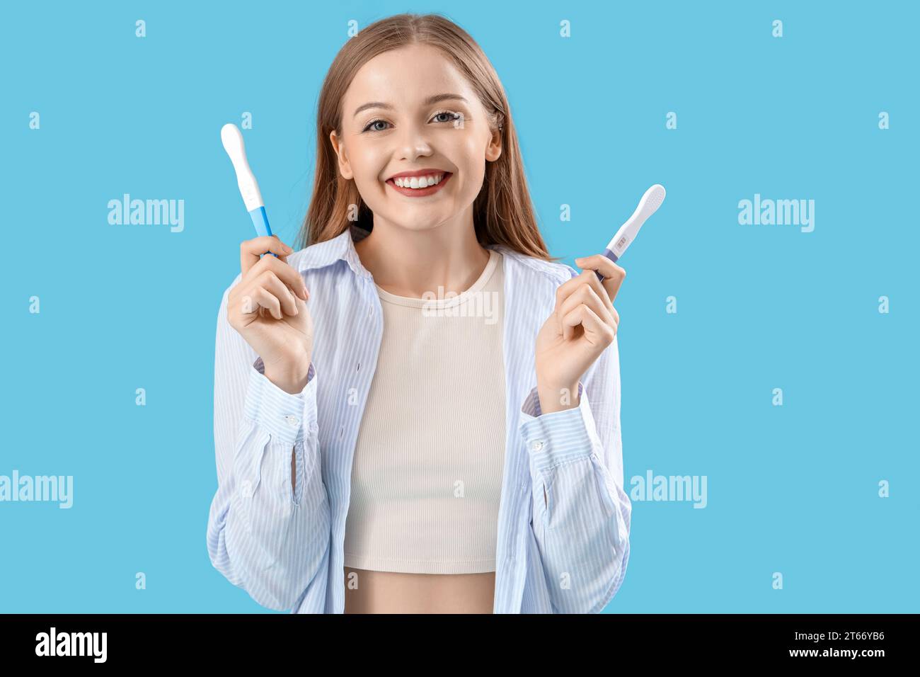 Jeune femme heureuse avec des tests de grossesse positifs sur fond bleu Banque D'Images