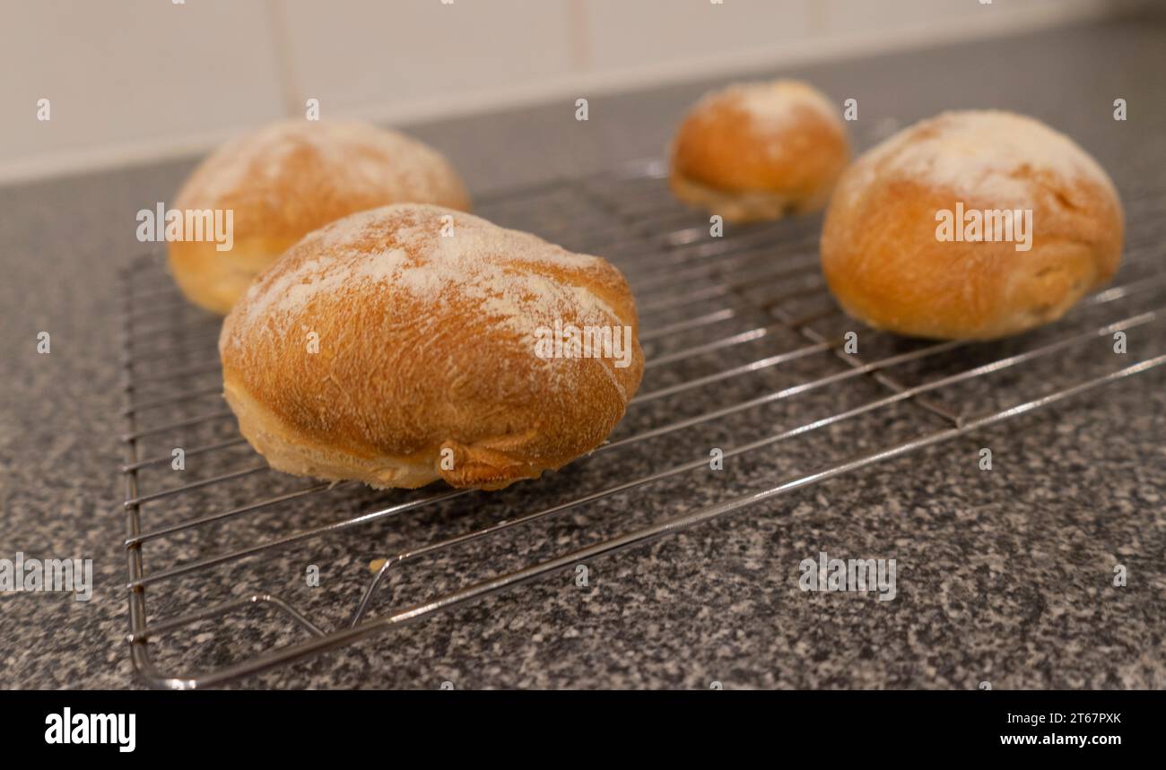 Quatre petits pains croustillants faits maison refroidissant sur une grille de refroidissement en acier inoxydable sur une surface de cuisine en marbre noir et blanc Banque D'Images