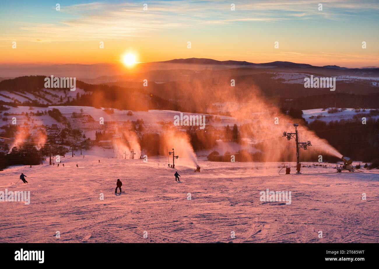 Piste de ski dans la station d'hiver avec des skieurs et des canons à neige au coucher du soleil, Slovaquie Banque D'Images