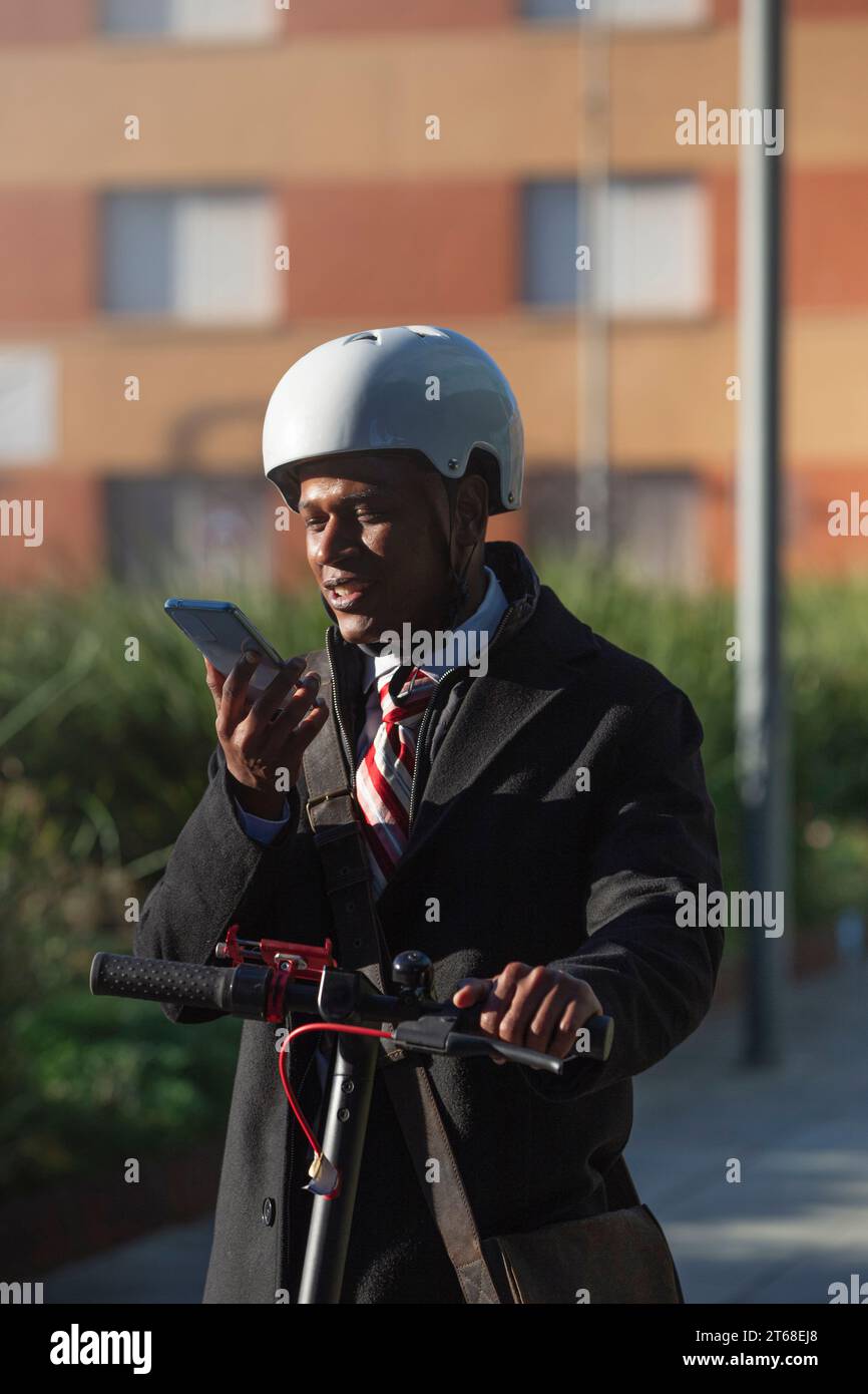 Un jeune homme dans une veste de costume professionnel et casque blanc debout sur un scooter et utilisant son téléphone portable Banque D'Images