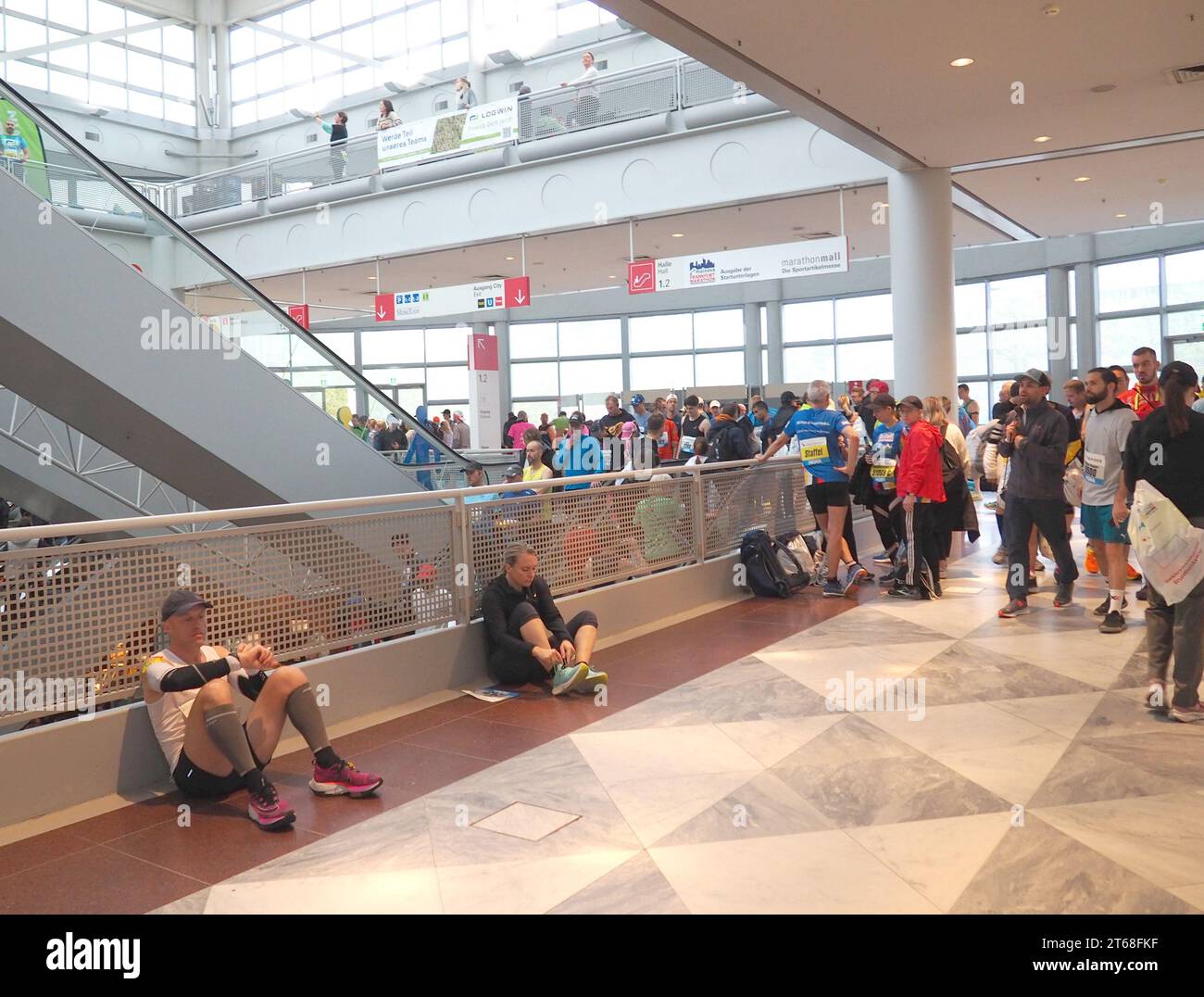 Coureurs en attente assis sur le sol dans le hall pour la préparation du marathon, homme regardant la montre de fitness, homme attachant des baskets, attente, événement , signes Banque D'Images