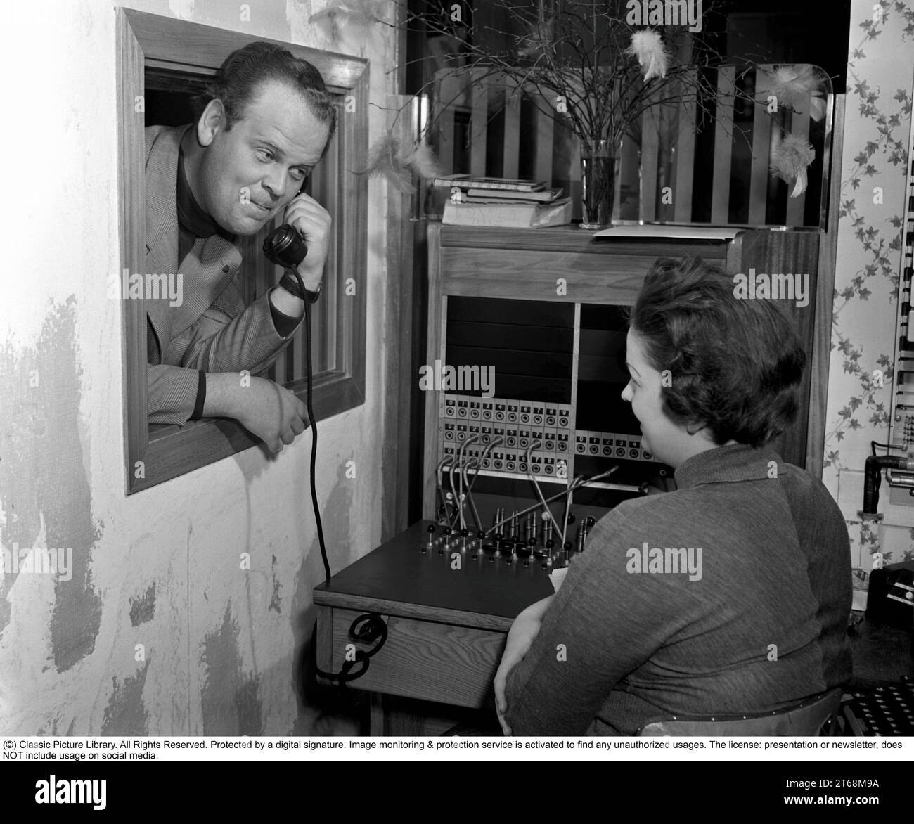 Arne Mattsson. 1919-1995, réalisatrice suédoise, connue pour avoir réalisé des films comme elle dansait un été, Hemsöborna et Körkarlen. Ici avec un récepteur téléphonique à l'oreille et une opératrice féminine qui travaille dans le standard de l'entreprise. Elle connecte les appels entrants et sortants à la bonne personne en utilisant des cordons pour les téléphones respectifs dans un standard téléphonique. Suède 1952 Kristoffersson ref 34k-40 Banque D'Images