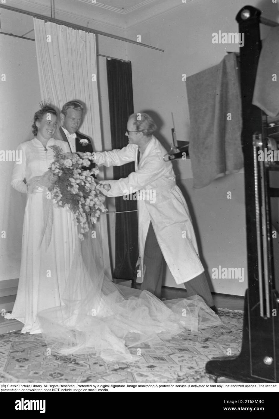 S'embrasser dans les années 1940 Couple de jeunes mariés Rohlsson ayant leur photo de mariage prise par un photographe professionnel dans un studio qui fait quelques ajustements aux arrangements floraux avant qu'il ne prenne les photos. Suède 1941 Kristoffersson Ref 199-16 Banque D'Images