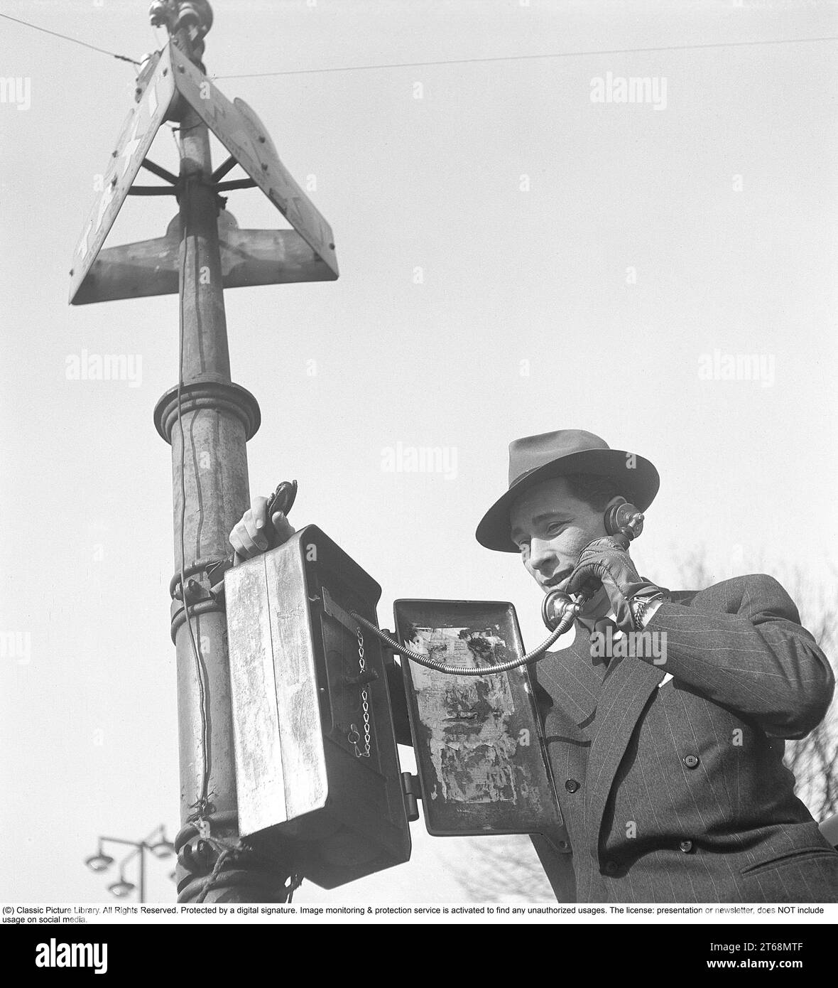 Taxi 1940s. Un homme habillé avec soin en costume et chapeau se tient devant un poteau de taxi à Stockholm et appelle un taxi. Dans le passé, il était courant qu'un téléphone directement relié au standard de taxi soit installé aux stations de taxis, s'il n'y avait pas de taxi là-bas, vous l'appeliez vous-même. Suède 1944. Kristoffersson réf. G73-2 Banque D'Images